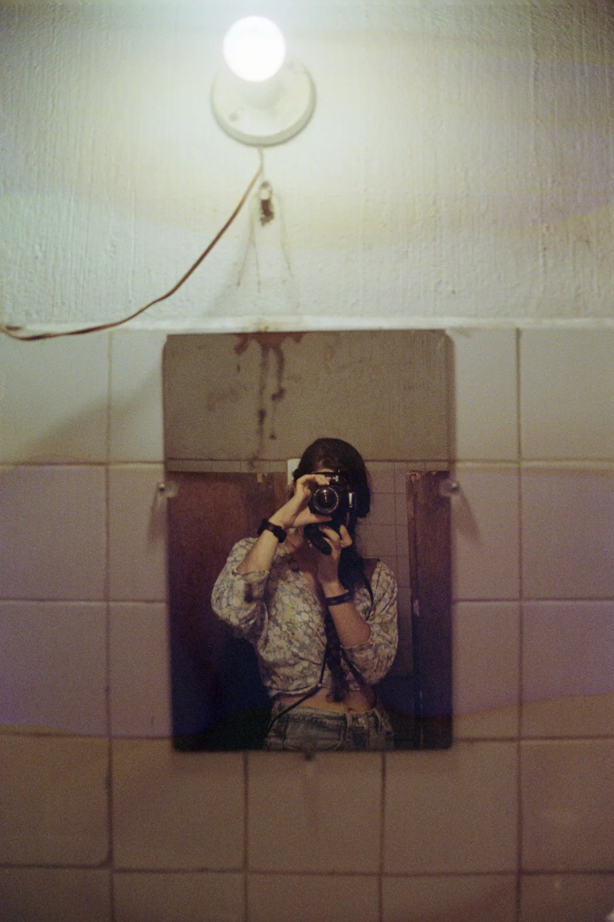 Carmen photographing her reflection in a tiled interior.